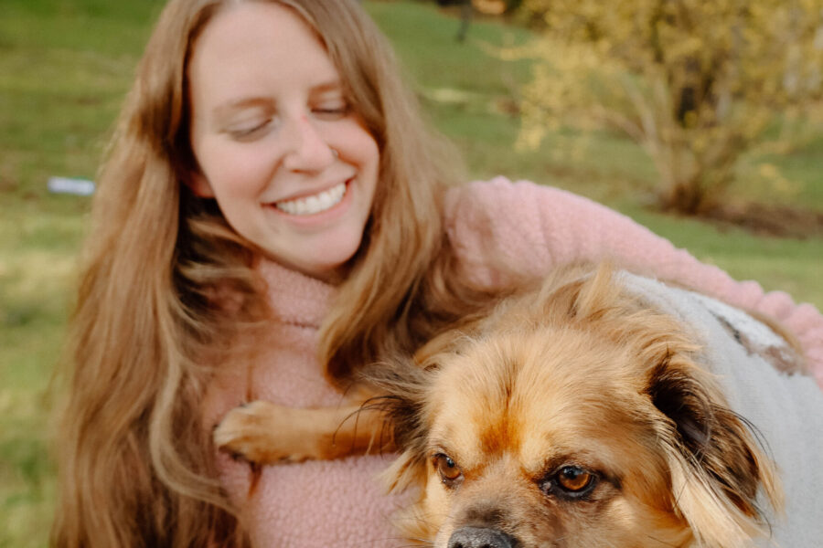 Lindsay smiling, holding a small tan dog outdoors